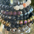 Stack of beaded bracelets with various colors and textures on a glass surface.