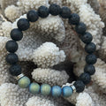 Black beaded bracelet with blue and green beads on a textured white background