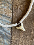 Closeup of Handmade shark tooth pendant necklace with 5mm puka shells, 18-inch choker style, displayed in natural light with coastal beach backdrop