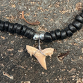 Black beaded necklace with a shark tooth pendant on a textured surface