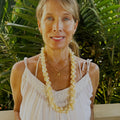Woman wearing a white dress and lei with green foliage in the background