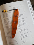 A collection of wooden bookmarks with Hawaiian inspired designs, featuring phrases and images related to Hawaii, displayed on a surface with a floral patterned book in the background.