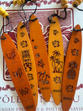 A collection of wooden bookmarks with Hawaiian inspired designs, featuring phrases and images related to Hawaii, displayed on a surface with a floral patterned book in the background.