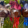 Decorative masks with feathers and beads hanging against a natural background