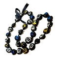 A black and gold, blue and silver kukui nut lei with a turtle pattern and an adjustable black ribbon closure.