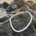 White shell necklace on a wooden log with a beach and sunset in the background
