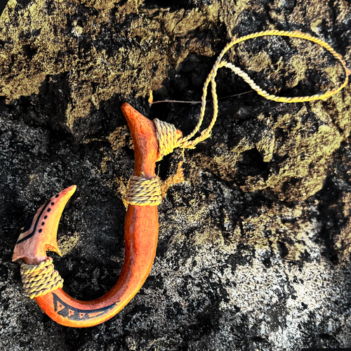 Wooden fish hook with yellow string on a textured rock surface