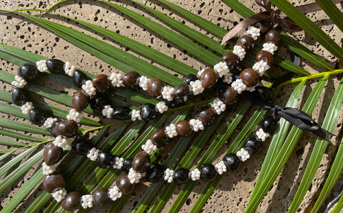 A Hawaiian lei necklace made of kukui nuts and white mongo shells, displayed on a green background.