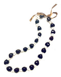 A black and pink kukui nut lei with a floral pattern and an adjustable black ribbon closure.