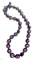 A black and pink kukui nut lei with a turtle pattern and an adjustable black ribbon closure.