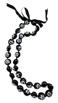 A black and silver kukui nut lei with a turtle pattern and an adjustable black ribbon closure.