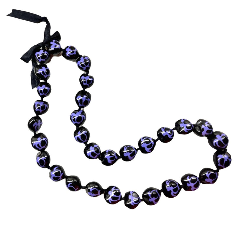 A black and purple kukui nut lei with a turtle pattern and an adjustable black ribbon closure.